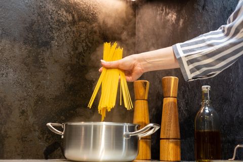 Nudeln passiv kochen: Eine Hand hält Spaghetti über einen Kochtopf
