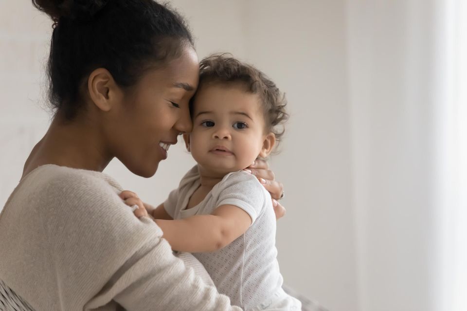 Entschleunigung: eine junge Frau legt ihre Stirn gegen das Köpfchen ihres Babys