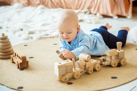 Baby liegt auf dem Boden und spielt mit einer Holzeisenbahn