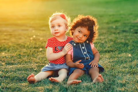 Erste Freunde: zwei kleine Mädchen sitzen nebeneinander auf dem Rasen