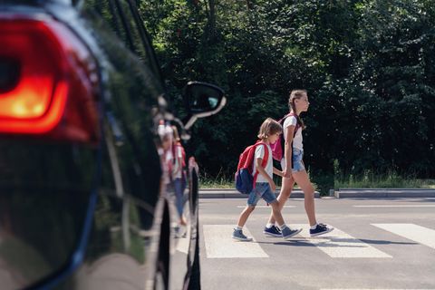 Risiko "Elterntaxi": Kinder überqueren einen Zebrastreifen vor einem Auto