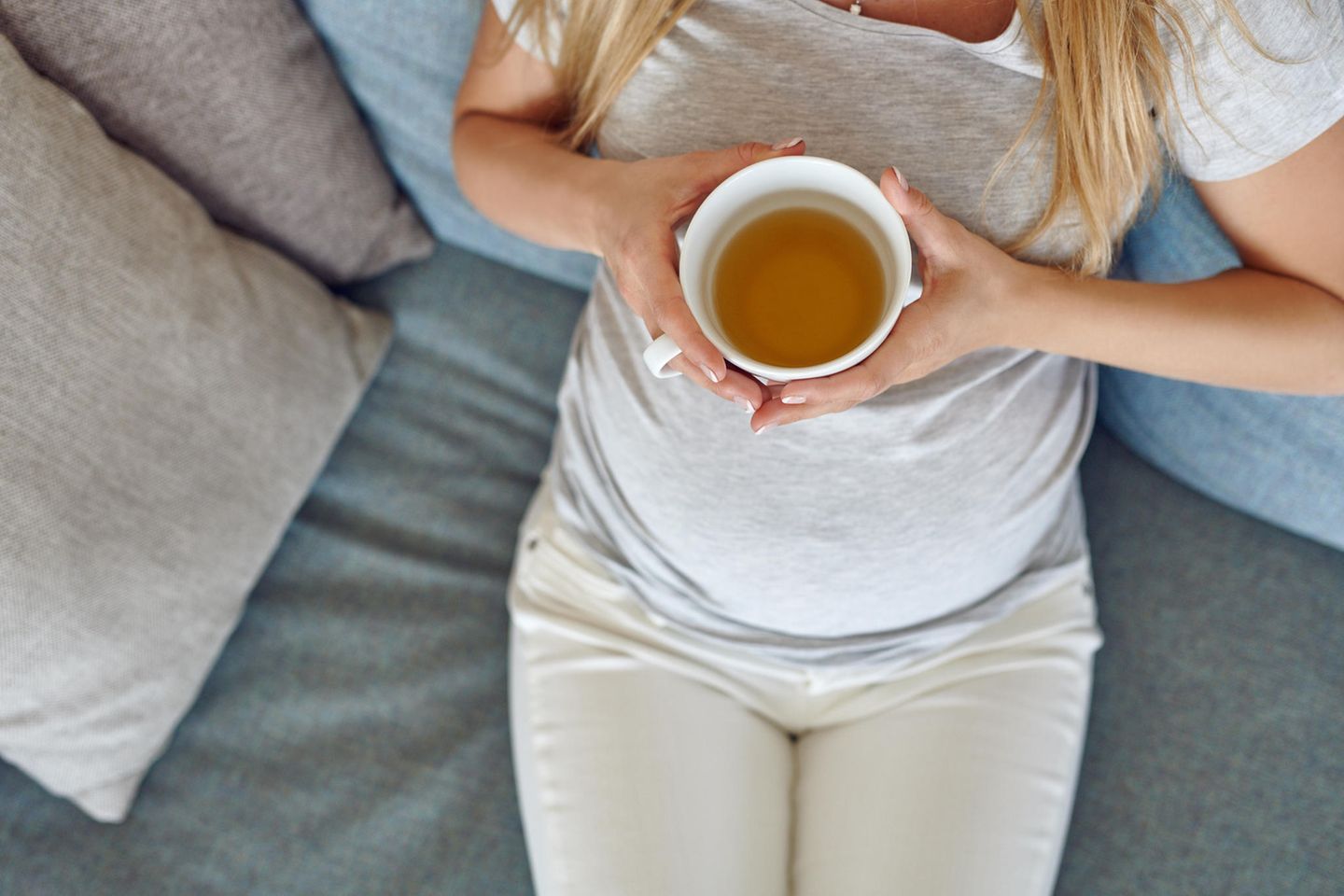 Grüner Tee in der Schwangerschaft: Schwangere liegt mit Tee auf dem Sofa