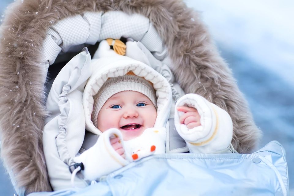 Ein Baby im Winter-Outfit lacht in seinem Kinderwagen