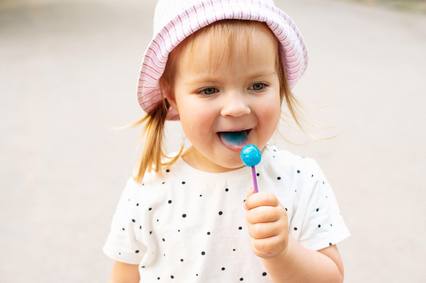 Auf süß geprägt: Ein kleines Mädchen leckt an einem blauen Lolli