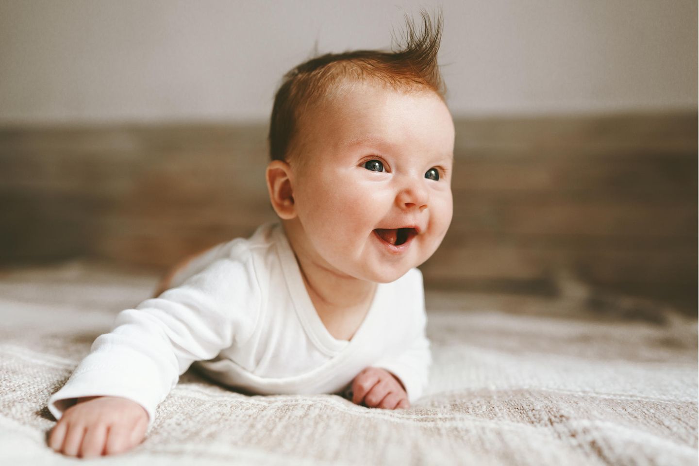 Raumtemperatur für Babys: Baby liegt lachend auf dem Boden