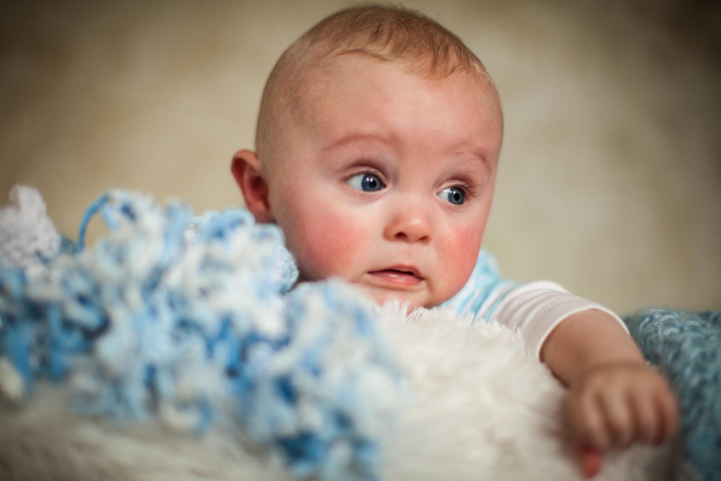 Baby mit roten Wangen liegt bäuchlings auf einer weichen Decke