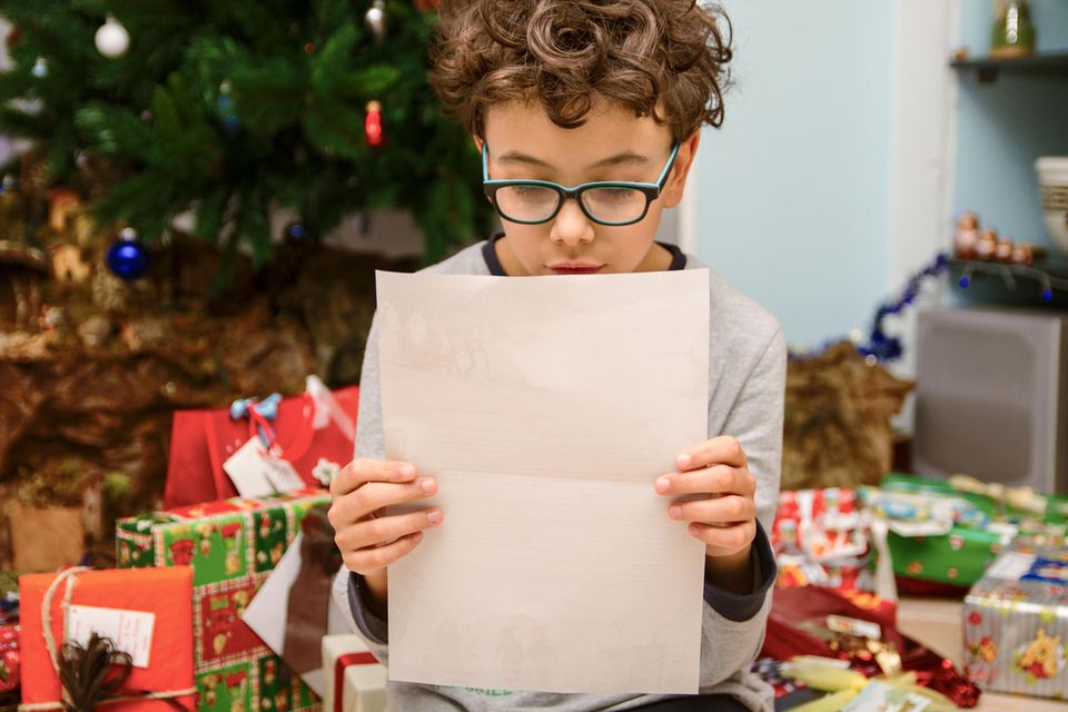 Kurze Weihnachtsgedichte: Kind liest von einem Blatt Papier vor dem Weihnachtsbaum
