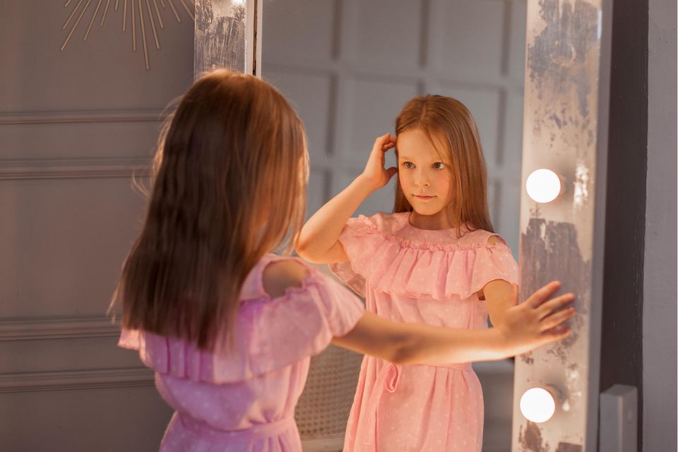 Negatives Körperbild: Ein junges Mädchen im rosa Kleid steht vor dem Spiegel
