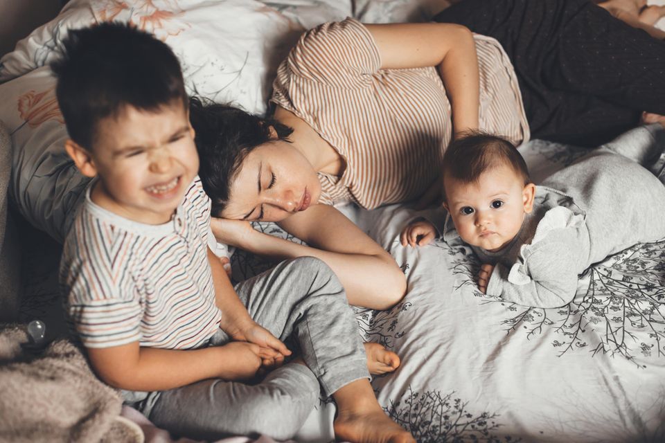 Eltern helfen Eltern: Mutter erschöpft mit Kindern im Bett
