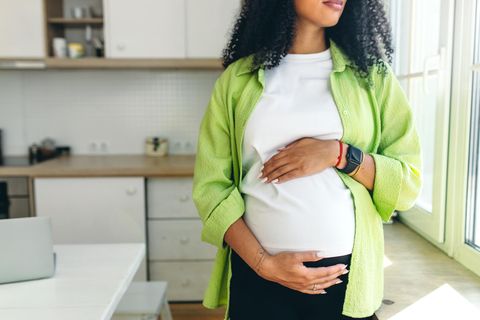 Der Babybauch wächst: Schwangere in hellgrüner Bluse hält sich oben und unten den Bauch