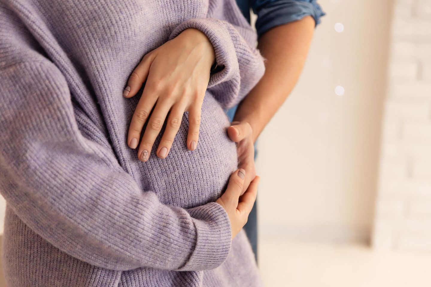 Herzförmige Gebärmutter: Frau und Mann berühren den Babybauch im fliederfarbenen Pulli