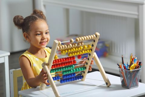 Spielzeug ab 6 Jahren: Lächelndes Mädchen spielt am Tisch mit einem Abakus.