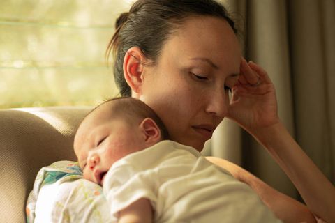 Eine nachdenkliche Frau hält ein schlafendes Baby im Arm