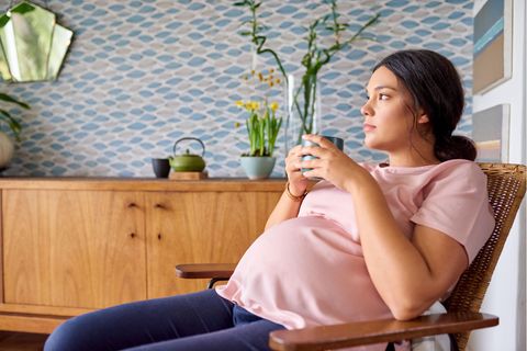 Mutterschaftsgeld: Schwangere Frau sitzt in einem Sessel und hält einen Becher