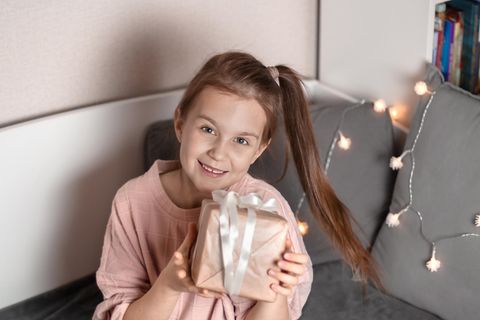 Sinnvolle Geschenke für 8-Jährige: Lächelndes Mädchen hält ein Geschenk hoch