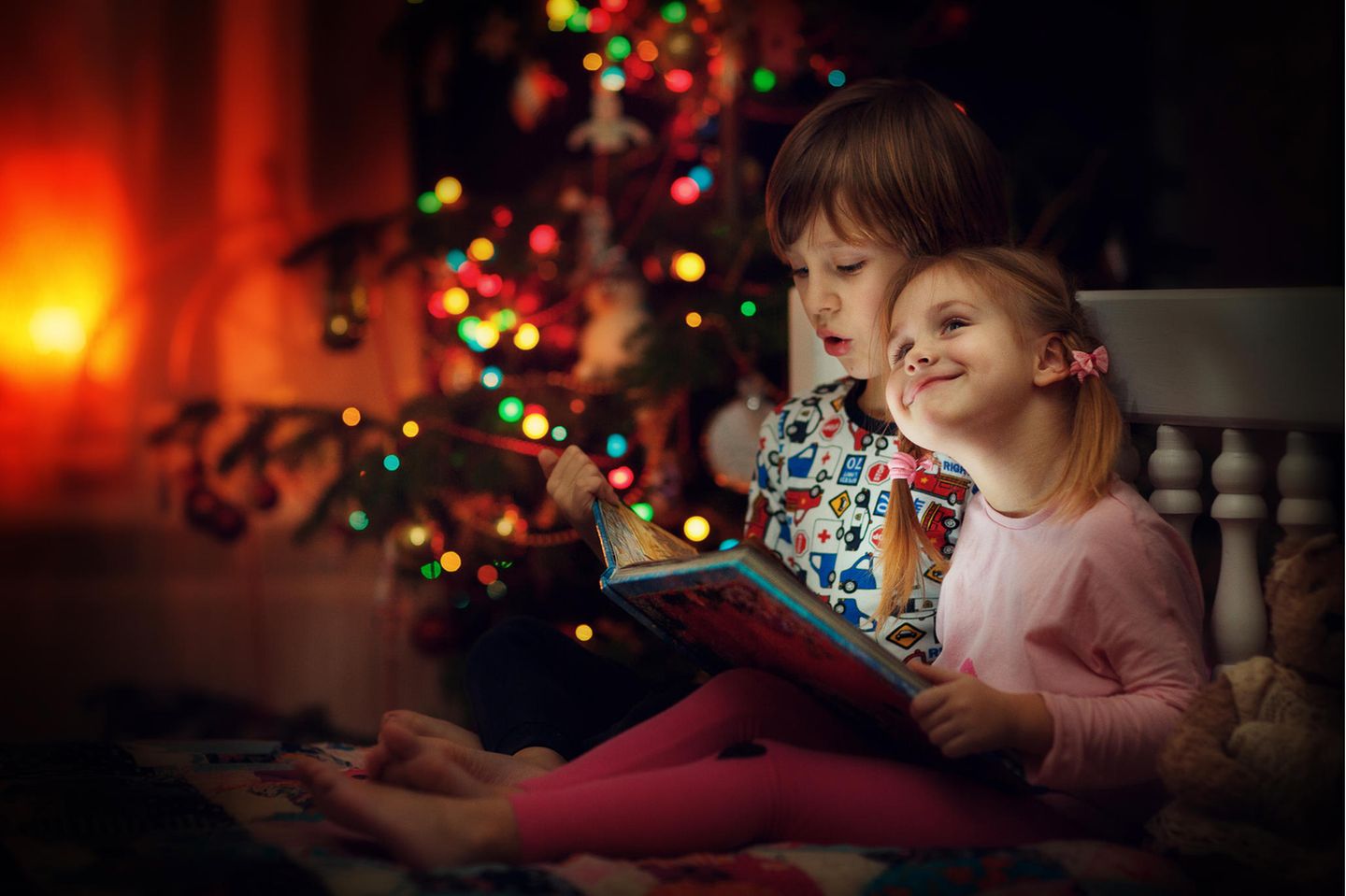 Zwei Kinder lesen unter einem Weihnachtsbaum ein Kinderbuch