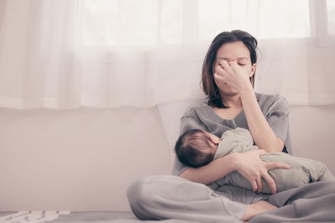 Vasospasmus beim Stillen: Frau stillt ihr Baby und hält sich die Hand vor das Gesicht