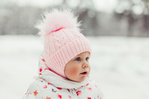 Niedliches kleines Mädchen mit rosa Wollmütze und roten Wangen im Schnee