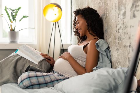 Schwangere Frau liest im Bett