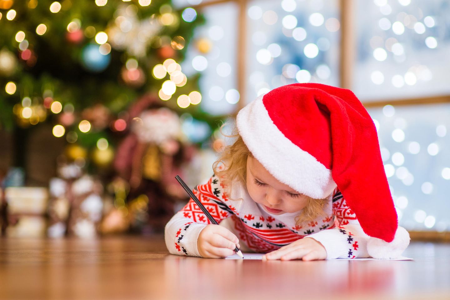 Adresse von Weihnachtsmann & Co.: Kind schreibt einen Brief vor dem Tannenbaum