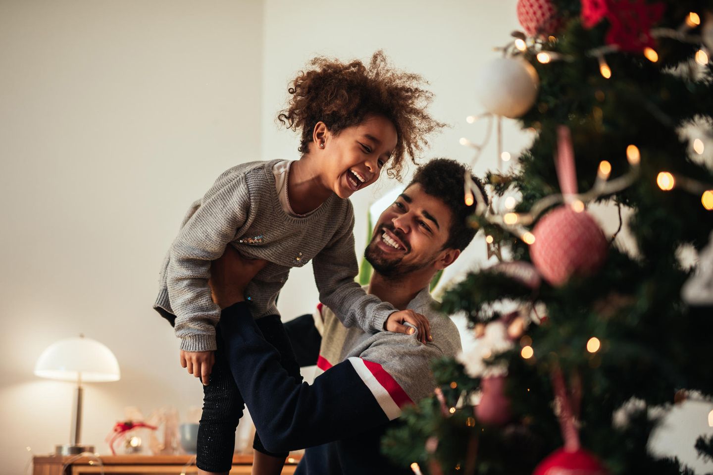 Vater lacht mit seinem Kind vor dem Weihnachtsbaum