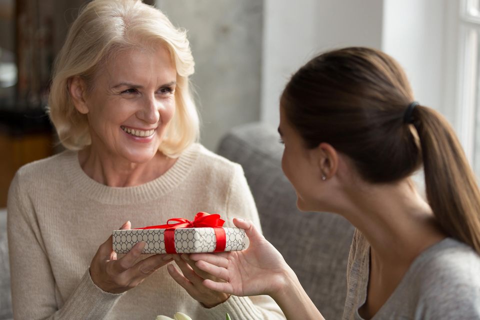 Geschenk für Schwiegermutter: Lächelnde ältere Frau bekommt ein Geschenk von einer jüngeren Frau.