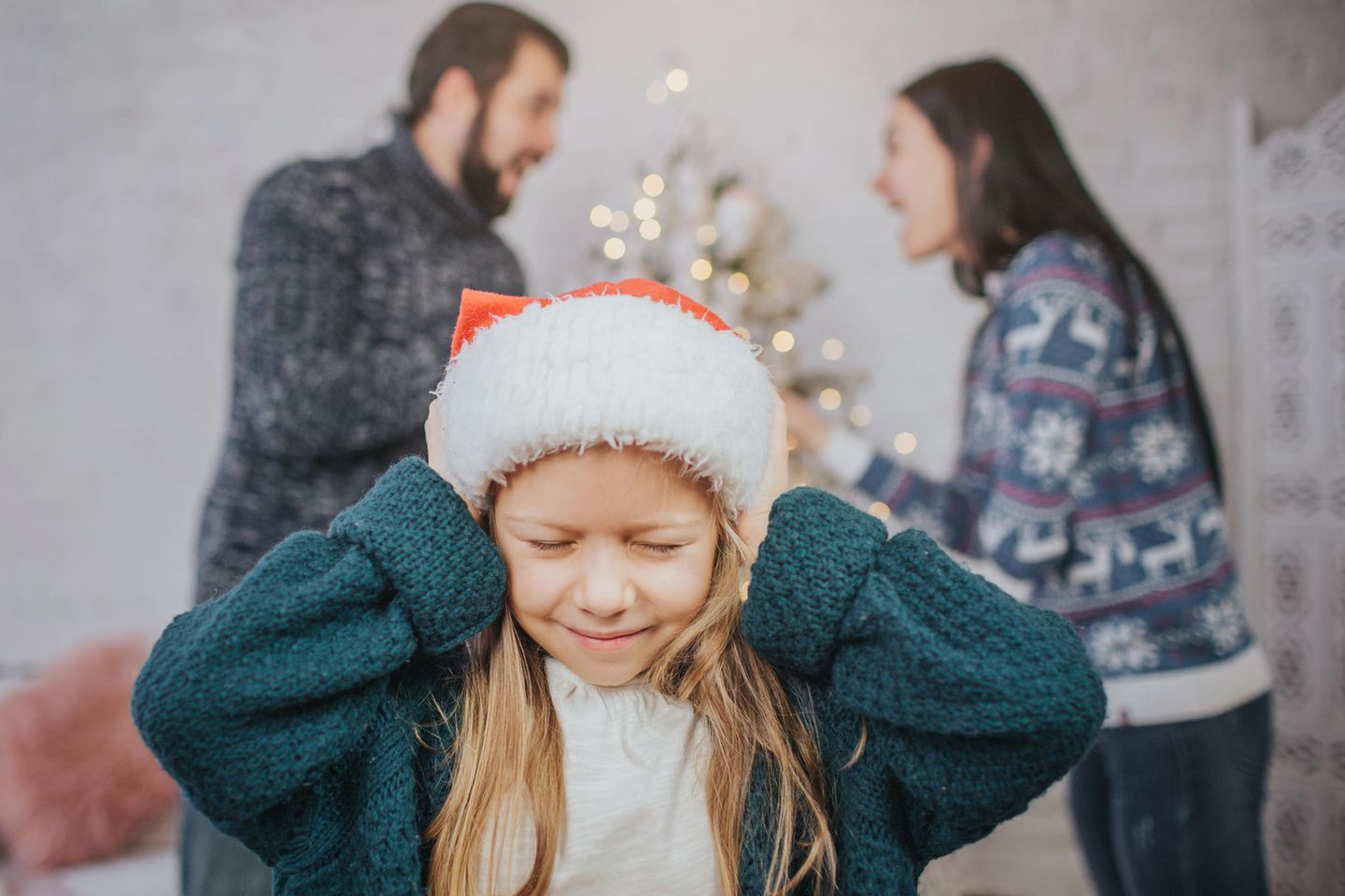 Weihnachten nach Trennung: Kind hält sich die Ohren zu und Erwachsenen streiten im Hintergrund