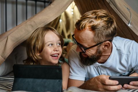 Spielzeug ab 6 Jahren: Kind spielt mit Vater im Zelt am Tablet.