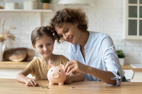 So geht Micro-Sparen: Mutter steckt Geld ins Sparschwein mit ihrer Tochter