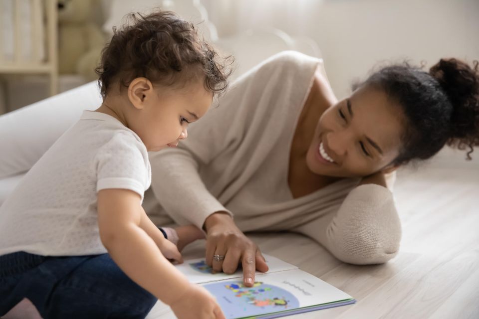 Kinderbücher ab 1 Jahr: Mutter und Kleinkind schauen auf dem Boden ein Bilderbuch an.