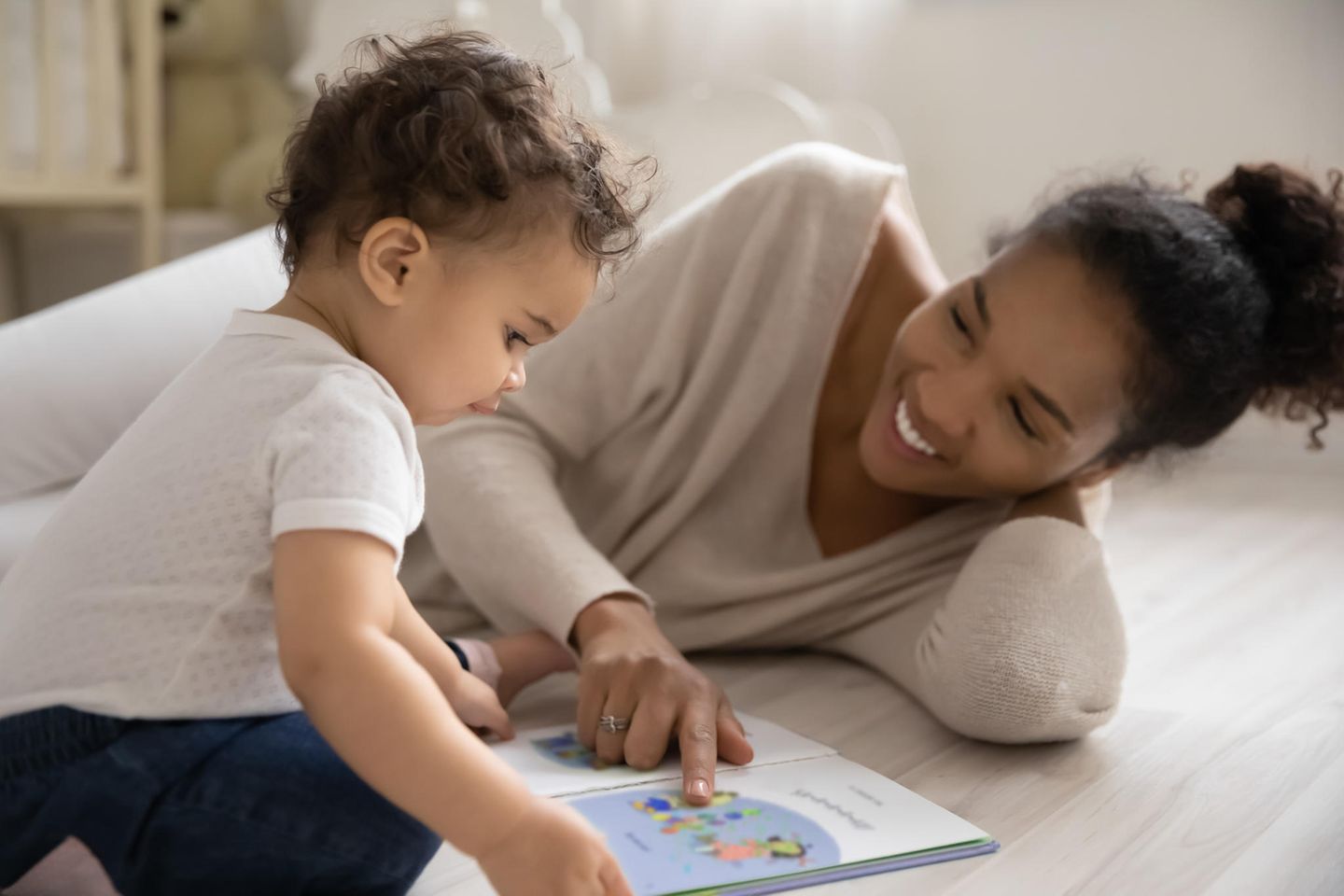 Kinderbücher ab 1 Jahr: Mutter und Kleinkind schauen auf dem Boden ein Bilderbuch an.