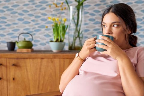 Hochschwangere Frau führt einen Teebecher zum Mund