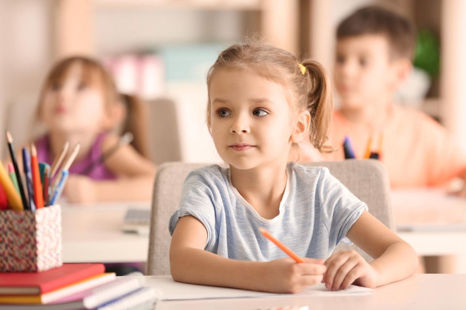 Kann-Kinder: Mädchen sitzt vor einem Blatt Papier mit Stift in der Hand