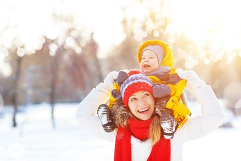 Frühkindliche Prägung: Frau trägt lachendes Baby im Schnee auf den Schultern