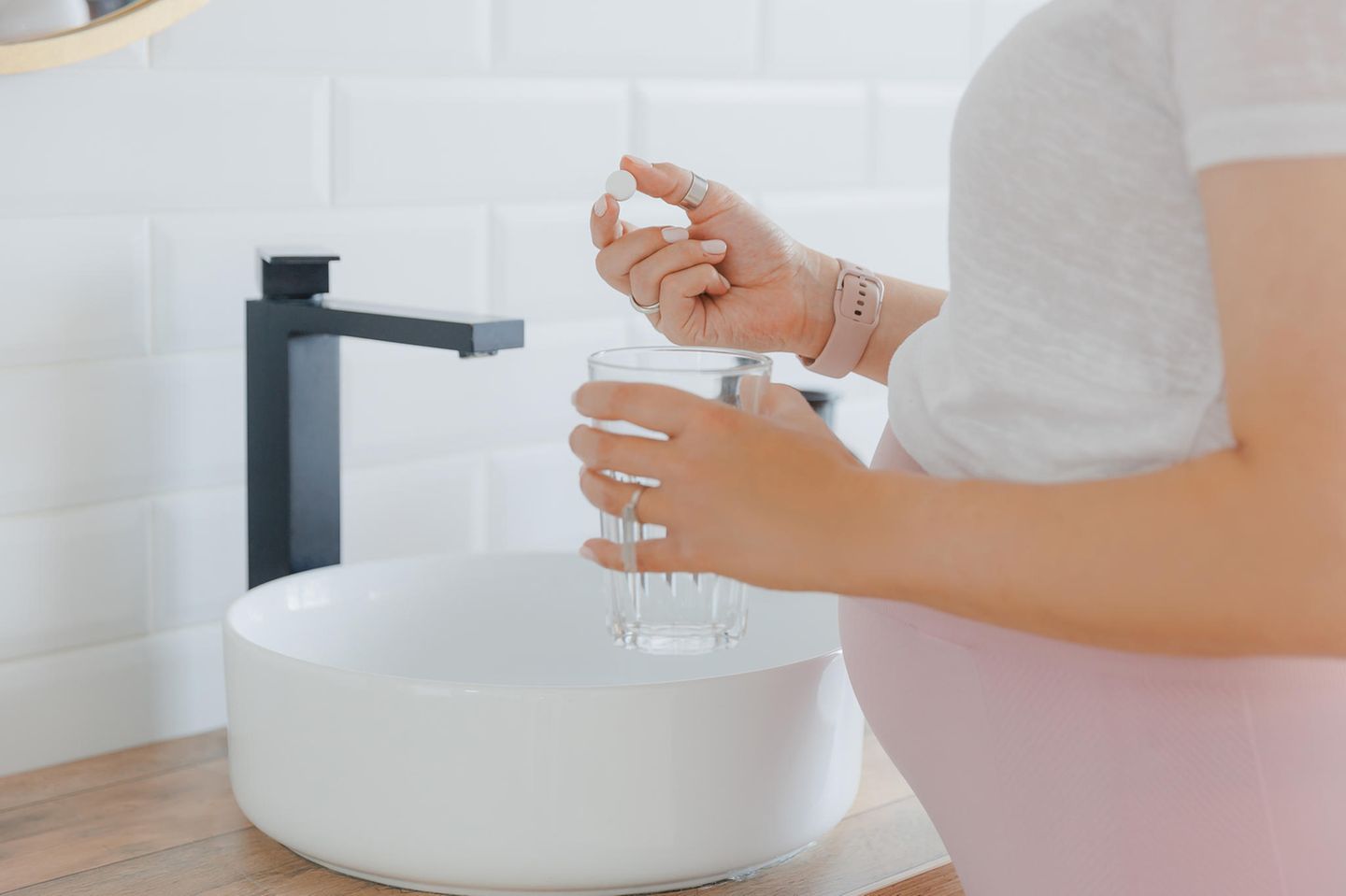 Welches Magnesium in der Schwangerschaft: Schwangere hält Wasserglas und Tablette in den Händen