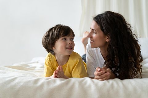 Mutter-Sohn-Beziehung: Mutter und Sohn liegen nebeneinader auf dem Bett und lächeln sich an