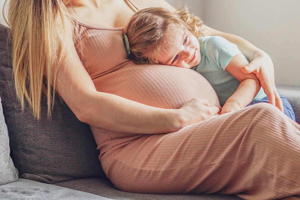 Fröhliches kleines Mädchen umarmt den schwangeren Bauch seiner Mutter