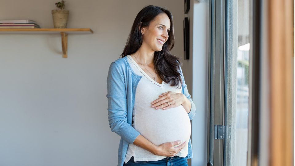 Schwangere Frau lächelt und hält ihren Bauch