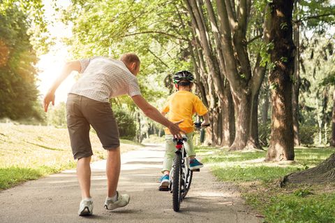 Fahrradfahren lernen: Mann übt mit Kind das Radfahren im Park