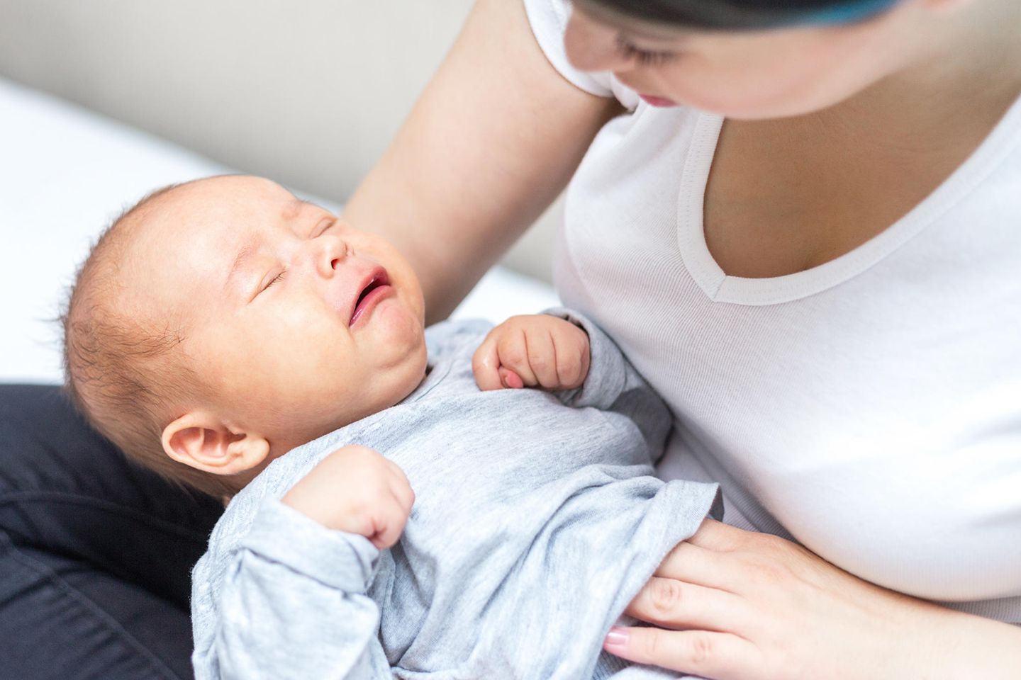 Kümmelzäpfchen für Babys: Frau legt weinendem Baby die Hand auf den Bauch