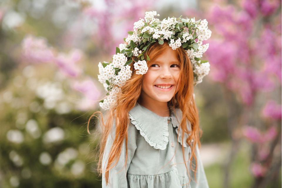 Rothaariges Mädchen mit Blumenkranz lacht in die Kamera