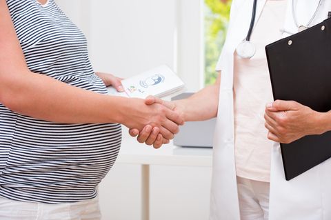 Mutterpass: Schwangere mit Mutterpass in der Hand begrüßt Ärztin