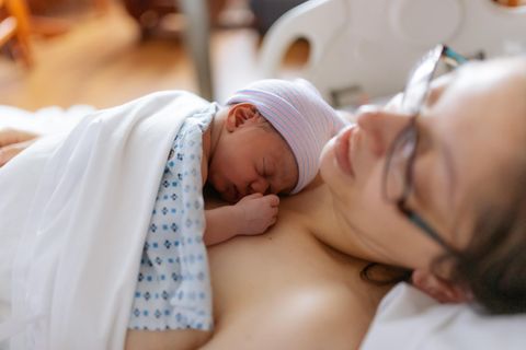 Nachwehen: Erschöpfte Frau liegt mit ihrem Baby auf einem Krankenhausbett