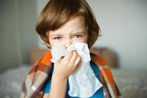 Erkältung: Kleiner Junge hat eine Decke über den Schultern und putzt sich die Nase