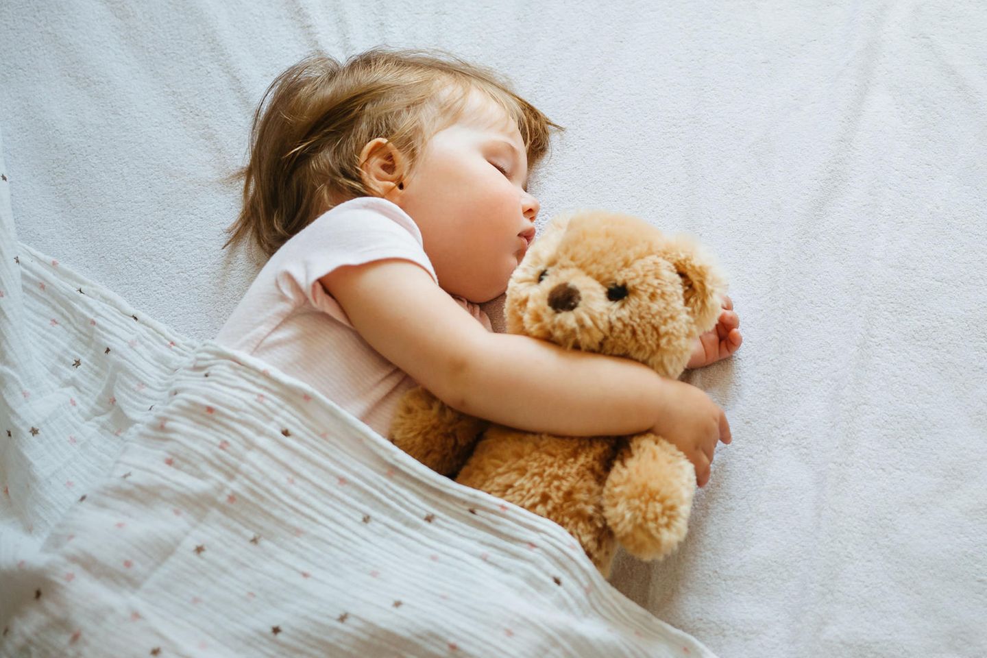 Wo schläft das Baby? Ein Baby schläft mit Teddy im Arm