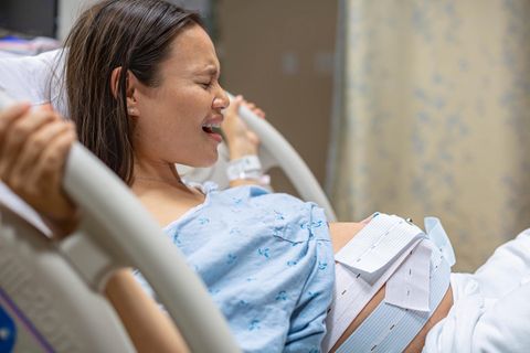 Wehensturm: Schwangere Frau liegt mit schmerzverzerrtem Gesicht auf einem Klinik-Bett