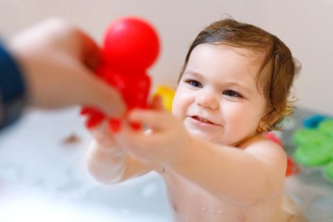 Badewannenspielzeug: Kleinkind greift fröhlich nach einem Badespielzeug