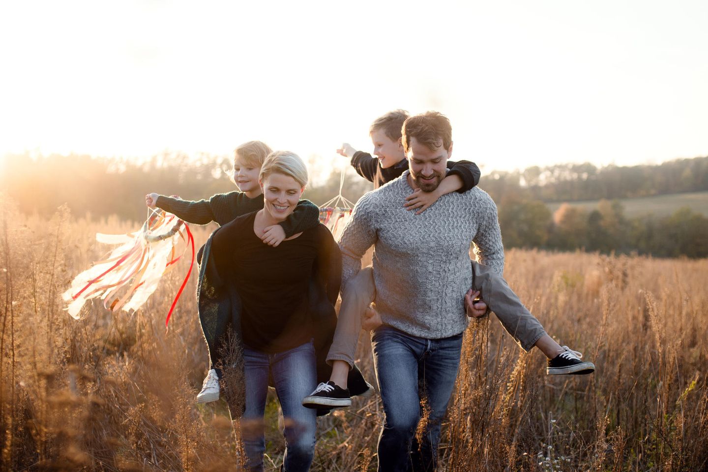 Co-Parenting: Mann und Frau tragen jeweils ein Kind auf dem Rücken und gehen über ein Feld