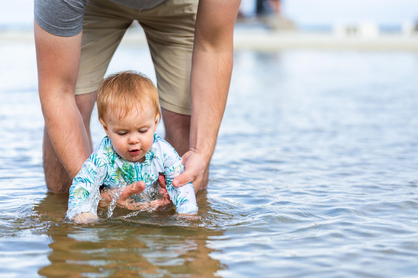 Sekundäres Ertrinken: Person hält ein Baby fest, das im flachen Wasser spielt