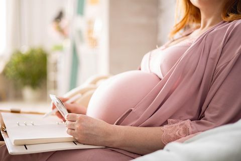 Schwangerschaftstagebuch: Schwangere Frau schreibt in ein Tagebuch und hält Ultraschallbild in den Händen